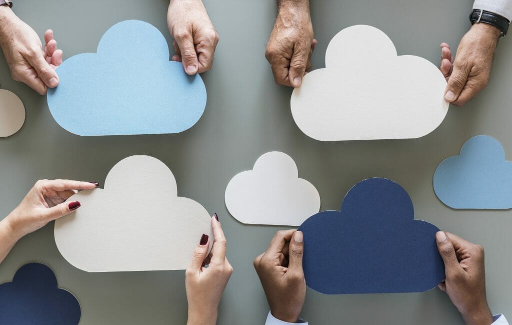 Hands holding cloud cutouts over gray background as imagery for cloud computing
