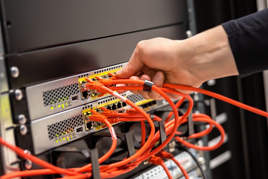 Cropped hand of male technician plugging network cable in router cluster at datacenter